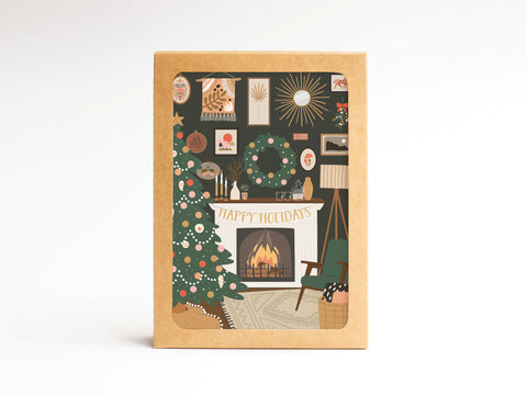 The Happy Holidays Cozy Fire Folded Greeting Note Set of 10 by Onderkast Studio features vibrant prints of a Christmas tree and wreath by the fireplace, with festive holiday artwork creating a cozy living room scene.