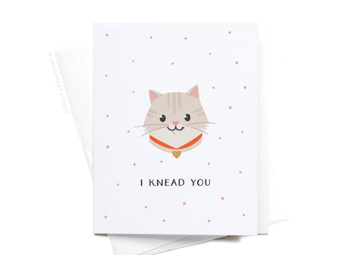 Onderkast Studios I Knead You Cat Greeting Card features a smiling cat in an orange collar with a heart tag, surrounded by pink polka dots, and the playful message I KNEAD YOU in vibrant colors—perfect for cat lovers.