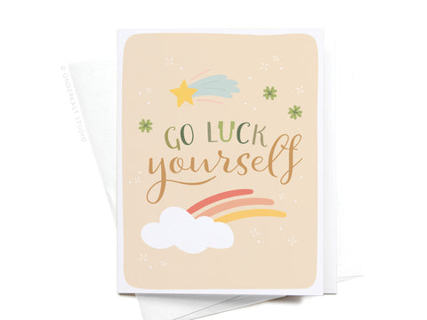 The Onderkast Studio Go Luck Yourself Greeting Card – FINAL STOCK features playful lettering, a shooting star, four-leaf clovers, clouds, and a rainbow on beige—a perfect good luck card for any occasion.