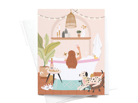 The Bubble Bath Cheers Greeting Card by Onderkast Studio features a charming woman savoring self-care in a bubble bath with cozy details—string lights, candles, plants, her cat and dog—perfect for celebrating relaxation and bliss.