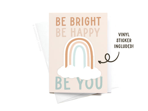 The Be Bright Be Happy Be You Rainbow Sticker Greeting Card by Onderkast Studio features a pastel rainbow and cloud design with vibrant lettering, includes a vinyl sticker, and comes with a white envelope.