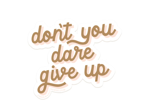 The Dont You Dare Give Up Sticker by Onderkast Studio features cursive light brown text with a white outline on white, made from durable, water-resistant vinyl for long-lasting inspiration wherever you stick it.