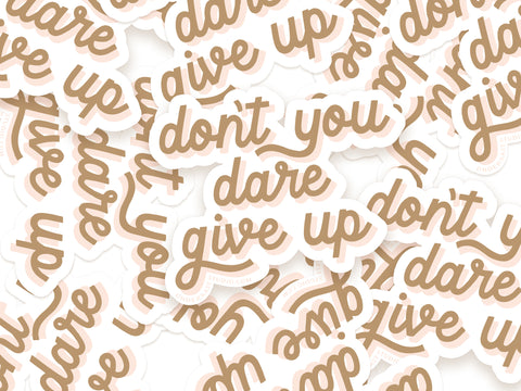 Onderkast Studios Dont You Dare Give Up Sticker features a handwritten brown phrase with a white outline, shown in a vibrant pile of overlapping stickers scattered randomly.