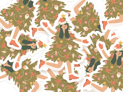 Onderkast Studio’s Christmas Tree Girl Stickers feature a smiling girl dressed as a festive tree with ornaments, star topper, and pink shoes. These durable, water-resistant vinyl stickers are shown scattered on a white background.