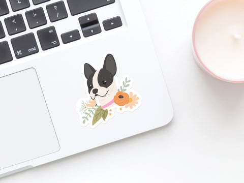 A close-up of a laptop with Onderkast Studios French Bulldog Floral Sticker—water and sunlight resistant vinyl—on the palm rest, next to a pink candle.