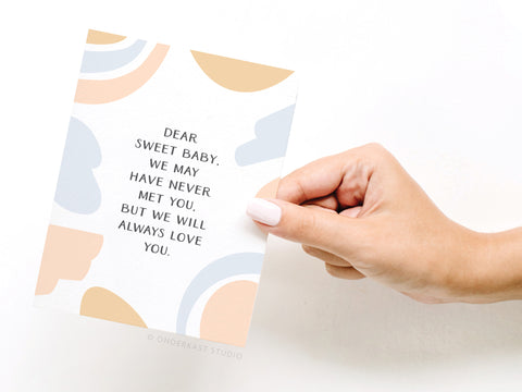 A hand with pale pink nails holds Onderkast Studios Dear Sweet Baby Miscarriage Greeting Card, featuring abstract pastel shapes and comforting words: Dear sweet baby, we may have never met you, but we will always love you.