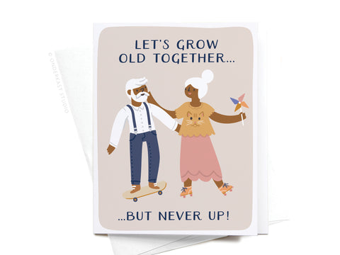 The Let’s Grow Old Together Greeting Card by Onderkast Studio features a dark-colored illustration of an elderly man on a skateboard holding hands with an elderly woman with a pinwheel, plus whimsical text—perfect for any fun-loving couple!.