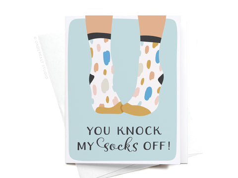 Send love with the You Knock My Socks Off Greeting Card – FINAL STOCK by Onderkast Studio, featuring colorful spotted socks and the phrase YOU KNOCK MY SOCKS OFF! on a light blue background. Premium quality—perfect for that special someone!.