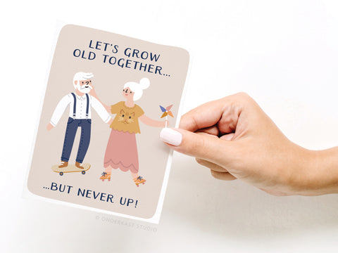A hand holds the Onderkast Studio “Let’s Grow Old Together Greeting Card,” featuring an elderly couple on roller skates holding hands, with “Let’s Grow Old Together... But Never Up!” above and below the illustration.