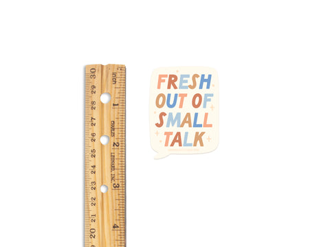 A wooden ruler rests next to the Onderkast Studio Fresh Out Of Small Talk sticker—a bold, colorful vinyl sticker thats perfect for introverts who appreciate quiet moments.