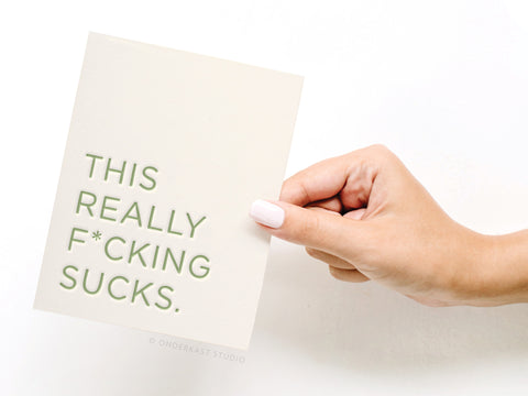 a hand holding a card that says, this really fucking sucks
